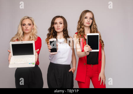 Drei Damen mit Gadgets. Drei wunderschöne elegante junge Frauen in lässig kleiden Stockfoto