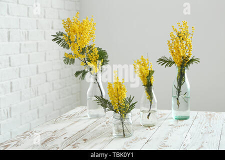 Glaswaren mit schönen Mimosa Blumen am weißen Tisch im Zimmer Stockfoto