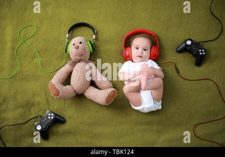 Adorable Baby Junge mit Teddybär, Kopfhörer und Joypads liegen auf weiches Plaid Stockfoto