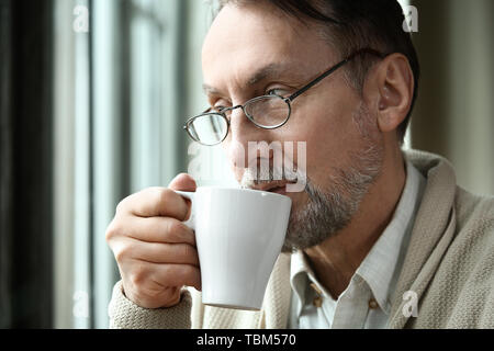 Stattliche reifer Mann Kaffee trinken in der Nähe der Fenster Stockfoto