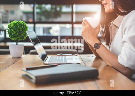 Asiatische arbeitende Frau mit Laptop und trinken Kaffee im Cafe. Die Menschen und Lebensstile Konzept. Technik und Wirtschaft Thema. Freiberufliche und Beruf t Stockfoto