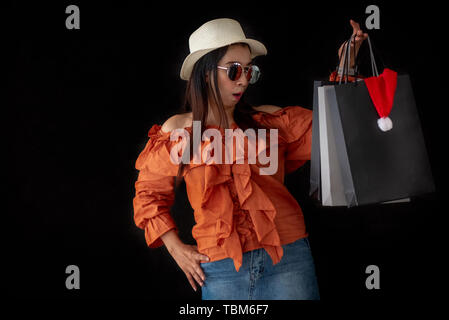 Asiatische Shopping Frau mit schwarzen Freitag Einkaufstasche und Santa Claus hat im Inneren auf schwarzem Hintergrund überrascht. Shopaholics und Schönheit mode Thema. Stockfoto
