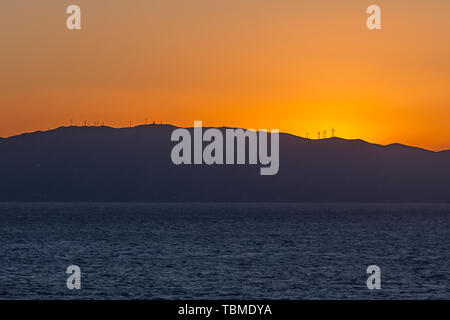 Sonnenuntergang hinter dem Profil einer Insel mit Windkraftanlagen Stockfoto