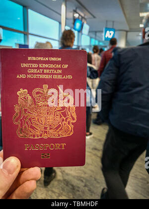 Einen weißen Mann hält seine roten britischen Paß in der Hand in der Mitte von einem überfüllten Abflugterminal Stockfoto