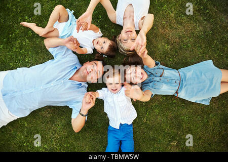 Gerne verspielt Familie, die auf dem Gras im Freien. die Eltern mit den Kindern im Sommer. Mama, Papa und Kinder Stockfoto