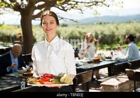 Positive Frau Kellner demonstrieren open-air Restaurant für Besucher Stockfoto