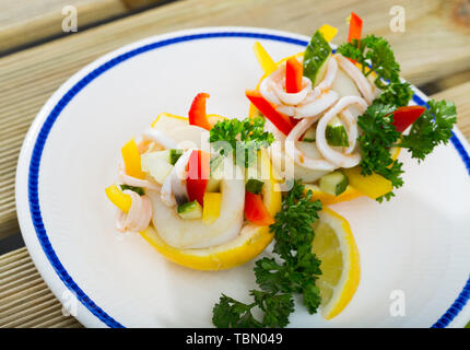Tropischer Salat mit Calamari, Gurken, rote Paprika, in Zitrone Hälften mit Olivenöl und griechischer Joghurt serviert. Stockfoto