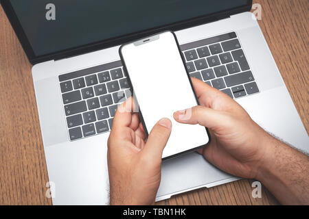 Mann mit Smartphone über das Laptop mit leerer Bildschirm. Technologie Werbung Konzept. Stockfoto