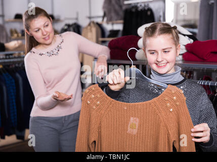 Jugendliche Mädchen eng am neuen Strickpullover suchen während des Einkaufs mit ihrer Mutter in der kleidung shop Stockfoto