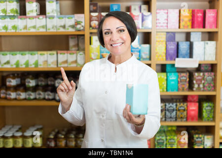 Lächelnd reife Frau Verkäufer Holding Box mit Nährstoffen bei gesunden Apotheke Stockfoto