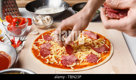 Chef Cooking Pizza. Hände Salami auf Pizza Base Stockfoto