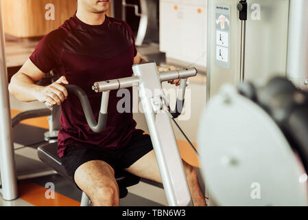 Vorderansicht des Sports Menschen mit Muskel dehnen Maschine namens sitzt Zeile in Fitness Gym. Menschen Lebensstil und Sport Training Konzept. Schließen bis vie Stockfoto