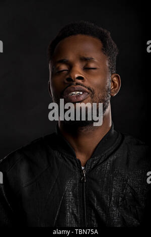 Closeup Portrait von einem Summenden entspannende afrikanische amerikanische Mann auf einem schwarzen Hintergrund mit geschlossenen Augen Stockfoto