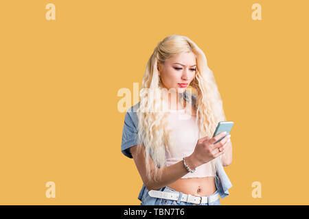 Schöne kaukasischen ernster Kursteilnehmer mit langen Haaren, in der Zelle Telefon, Videokonferenz, News lesen, über wireless Internet auf Gelb b Stockfoto