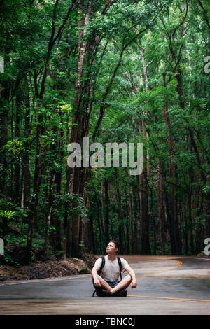 Mann mit Rucksack sitzt auf der Straße durch grünen Wald Bilar Man-Made, Bohol, Philippinen Stockfoto