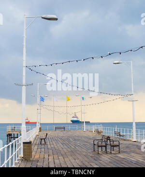 Hölzerne Seebrücke in Limassol Promenade. Indusrtial Frachtschiffe im Hintergrund. Zypern Stockfoto