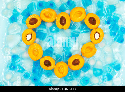 Herz aus reifen Aprikosen mit oder ohne Steine vor dem Hintergrund transparent und blau Eiswürfel mit kopieren. Ansicht von oben. Frische Früchte. S Stockfoto