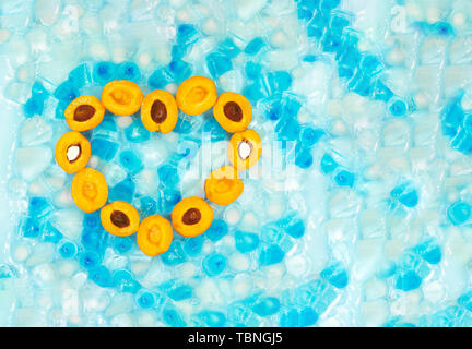 Herz aus reifen Aprikosen mit oder ohne Steine vor dem Hintergrund transparent und blau Eiswürfel mit kopieren. Ansicht von oben. Frische Früchte. S Stockfoto
