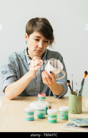 Die Töpferei Frau hält in der Hand einen Becher das Ornament zu malen, handgefertigte Keramik Stockfoto