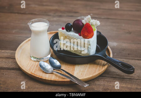 Süßes Obst Torte geschnitten servieren mit Milch Glas auf Holzplatte mit niedriger Beleuchtung eingestellt. Stockfoto