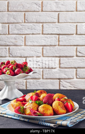 In der Nähe von Cottage cheese Donuts mit Erdbeeren auf einem Schild an einer konkreten Tabelle. Obstkorb mit frischen Erdbeeren im Hintergrund vor einer Stockfoto