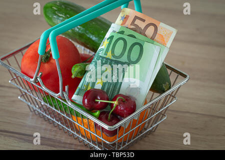 Gemüse und Früchte in den Warenkorb zusammen mit Euro Geld / das Konzept der Nahrungsmittelpreise erhöhen Stockfoto