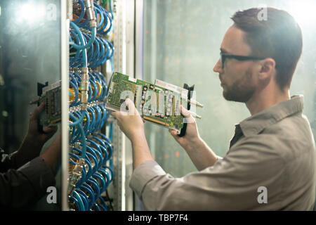 Ernsthafte konzentrierte junge Bartgeier server Reparatur professionelle in Gläsern stehen im Kabinett von Server Racks und Installieren von Hardware im Rack Stockfoto