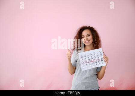 African-American woman holding Kalender mit markierten Tagen der Menstruation auf farbigen Hintergrund Stockfoto