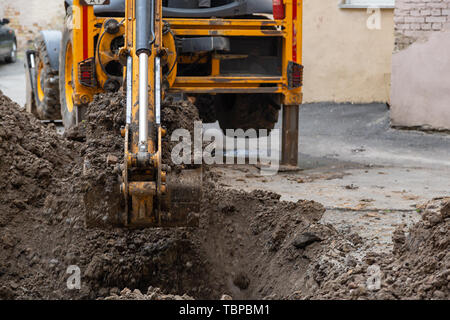 Bagger gräbt ein Graben. Reparaturarbeiten im Innenhof eines Wohnhauses. Stockfoto