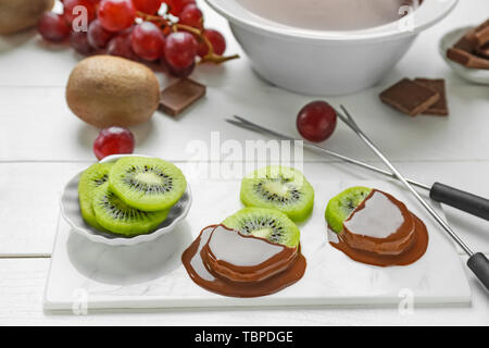 Frische kiwi Scheiben mit geschmolzener Schokolade am weißen Tisch Stockfoto