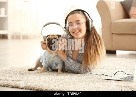 Junges Mädchen mit niedlichen Mops hund Hören von Musik zu Hause. Stockfoto