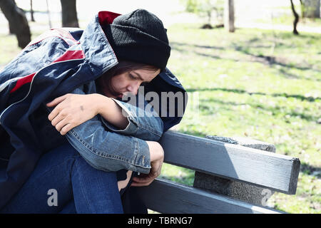 Arme obdachlose Frau sitzt auf der Bank im Freien Stockfoto