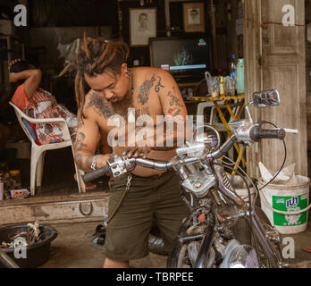 Lampeng, Tahiland - 2019-03-07-Mann mit vielen Tattoos Reparaturen sein Motorrad. Stockfoto