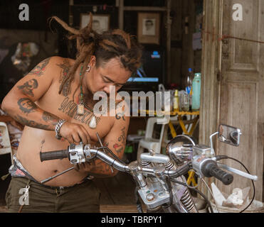 Lampeng, Tahiland - 2019-03-07-Mann mit vielen Tattoos Reparaturen sein Motorrad. Stockfoto