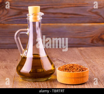 Sesamsamen in der Schüssel und eine Flasche Öl mit Cork auf hölzernen Tisch Stockfoto