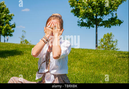 Schöne boho style Frau mit Zubehör genießen Sie den Sommer auf sonniger Tag im Park. Weibliche Hände mit Armbänder und Ringe auf ihrem Gesicht. Stockfoto