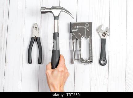 Hand mit einem Hammer. Werkzeuge, Schraubenschlüssel und Zangen auf weißem Holz- Hintergrund Stockfoto