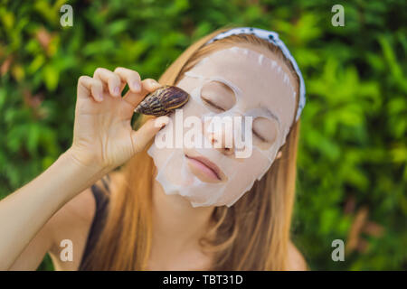 Eine junge Frau macht eine Gesichtsmaske mit Schnecke Schleim. Schnecke kriecht auf einer Maske Stockfoto