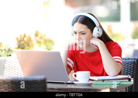 Sorgen Schüler e-Learning anschauen Tutorials auf Laptop in einem Café Terrasse sitzen Stockfoto