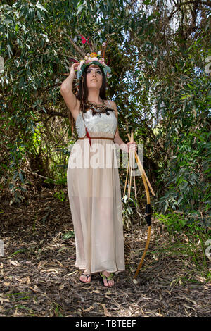 Ein Mädchen im Kleid Pocahontas mit Bogen und Pfeil auf der Suche vor dem hintergrund der grünen Laub Stockfoto