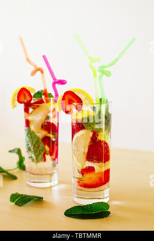 Erfrischend lebendige Sommer Getränke mit Zitrone, Erdbeere und Minze und bunte Strohhalme auf dem hölzernen Tisch Stockfoto