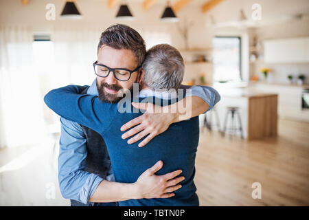 Ein erwachsener Sohn und Vater in Innenräumen zu Hause, umarmen sich. Stockfoto