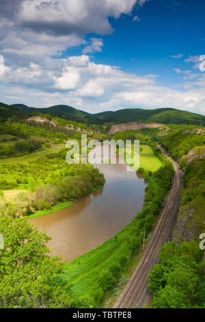 Blick vom Hügel in das Tal mit dem Fluss Berounka. Fluss Berounka, Kalksteinfelsen, Wiesen, Felder und Eisenbahn. Stockfoto