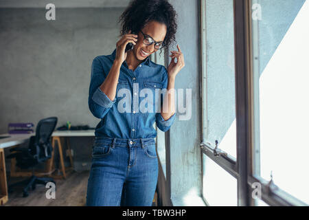 Geschäftsfrau Gespräch am Handy und lächelnd. Weibliche Unternehmer stehen durch ein Fenster und Sprechen über Handy im Büro Stockfoto