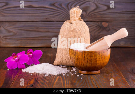 Meersalz in Löffel aus Holz und Schale, Blume und Sackleinen schlecht auf hölzernen Hintergrund Stockfoto