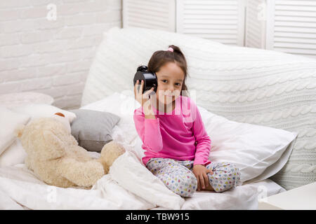 Süßes kleines Kind Mädchen im Schlafanzug mit Uhr im Bett. Guten Morgen Stockfoto