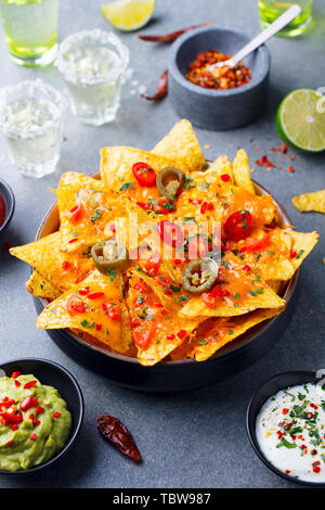 Nachos Chips mit geschmolzenem Käse und Dips Vielfalt in schwarz Schüssel. Grauen Stein Hintergrund. Stockfoto