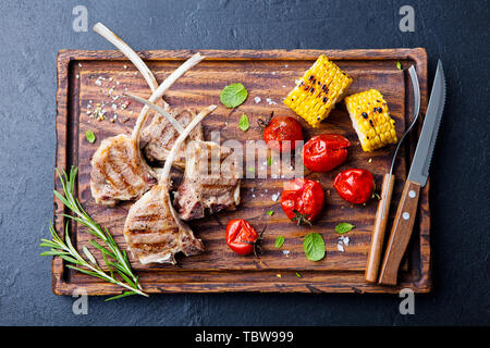 Lamb Ribs vom Grill auf Schneidebrett mit gebratenem Gemüse. Ansicht von oben. Stockfoto