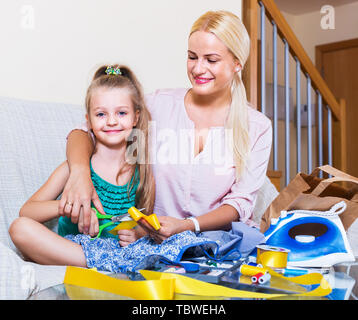 Lächelnde Mutter Lehre kleine Tochter drinnen zu nähen. Fokus auf Mädchen Stockfoto