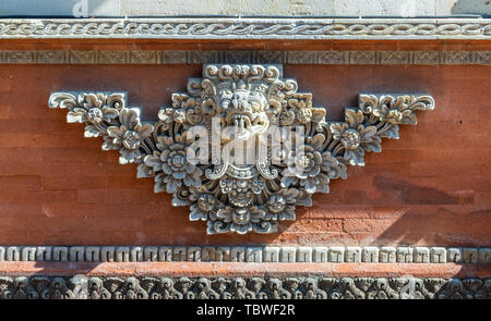 Ubud, Bali, Indonesien - 26. Februar 2019: batuan Tempel. Nahaufnahme des grauen Stein Ornament auf roten Ziegeln von Monster Kopf und Blumen. Stockfoto